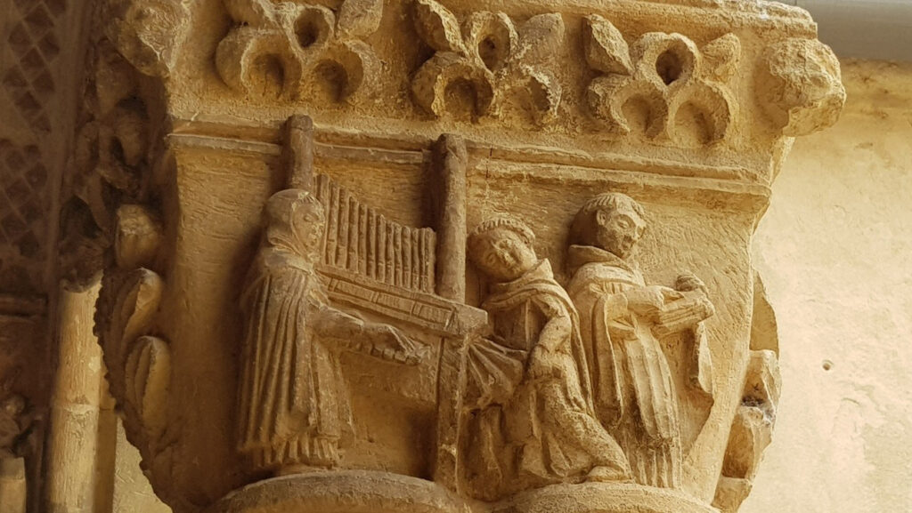 Podemos ver a tres frailes: uno tocando el órgano, otro dando aire al instrumento con el fuelle y el tercero leyendo la letra.