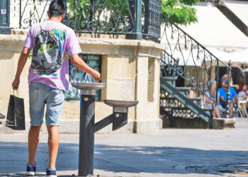 Una persona se refresca en una fuente durante un día de calor.