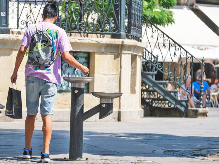 Una persona se refresca en una fuente durante un día de calor.