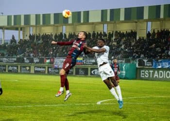 Marc Tenas intenta peinar un balón ante la oposición de un contrario. Al fondo, la grada prácticamente llena de aficionados./ HÉCTOR CRIADO