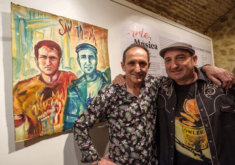 A la izquierda, Kike, con gorra, y José posan junto a un retrato suyo expuesto en el Torreón de Lozoya durante la muestra ‘Arte y música’ con la que se celebró el trigésimo aniversario del Bar Santana en 2022.