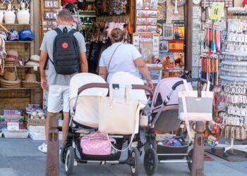 Una pareja con varios carritos de bebé frente a una tienda.